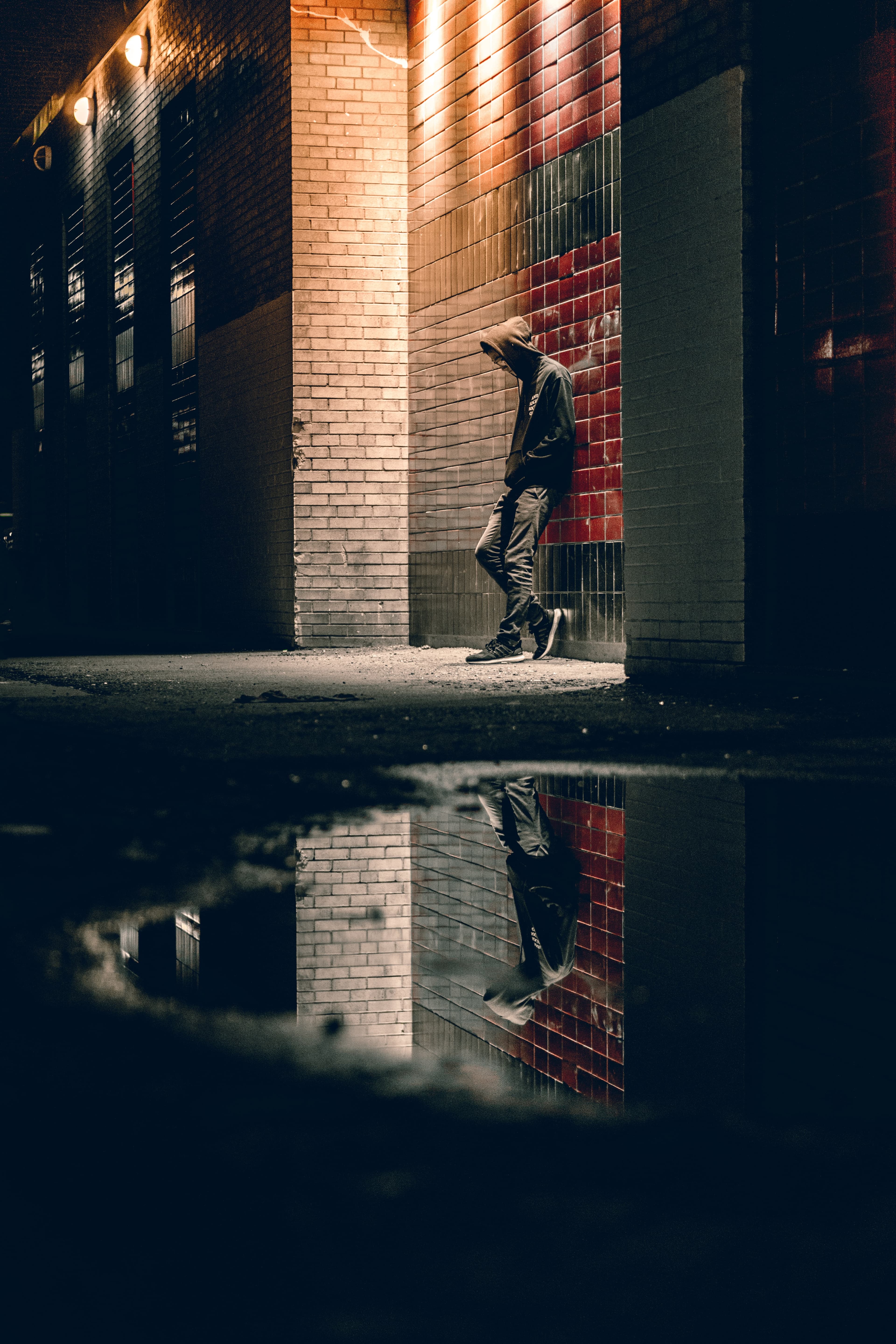 Man in hoodie leaning against wall looking at ground. Photo by @wflwong on Unsplash.com